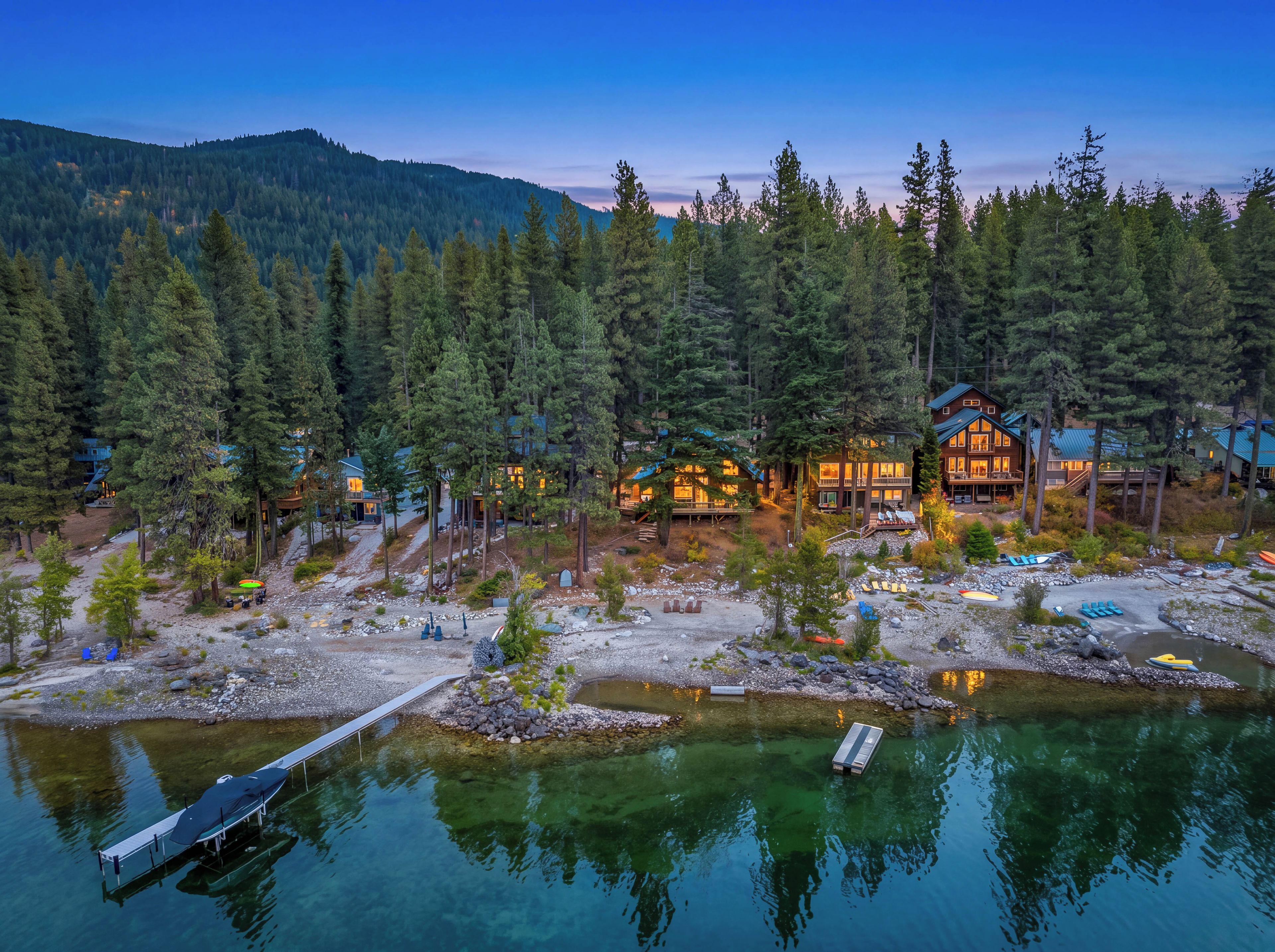 Un chalet au bord du lac, doté de plusieurs cabanes, d’un quai et offrant une vue dégagée sur la forêt environnante.