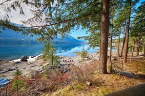 A mountainous landscape with a lake, trees, and a wooden deck. - Lakeside Retreat w/Private Sandy Beach and Hot Tub (Leavenworth)