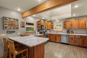 A modern kitchen with wooden cabinets, a marble island, and a clock on the wall.