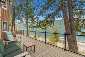 Eine Holzterrasse mit Gartenmöbeln, mit Blick auf einen See, umgeben von Bäumen.
