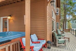 Een houten terras met een jacuzzi, rode en groene loungestoelen, en uitzicht op een meer.