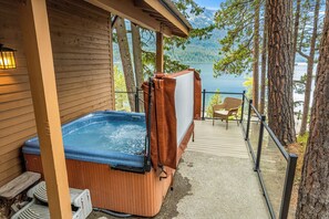 Un jacuzzi al aire libre frente a una cabaña de madera con vista a un lago y montañas.
