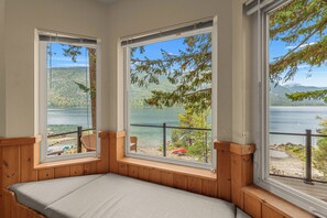 Ein Zimmer mit einem Bett, zwei Fenstern und Blick auf einen See und Wald.