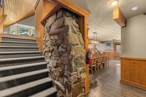 Una escalera con pared de piedra, vigas de madera y un área de comedor con sillas y una mesa.