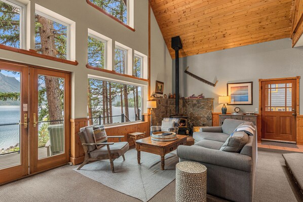 A spacious living room with a stone fireplace, large windows, and a view of a lake.