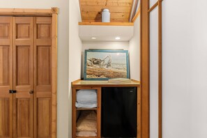 Ein Zimmer mit einer Holztür, einem gerahmten Kunstwerk auf einem Regal, einem kleinen schwarzen Gerät und einem weißen Handtuch.