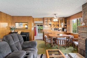A living room with a sofa, a dining table with chairs, a kitchen area with cabinets and a refrigerator, and a piano. - Downtown Historic Guesthouse, 3 Queens, Parking, Pets Welcome (Leavenworth)