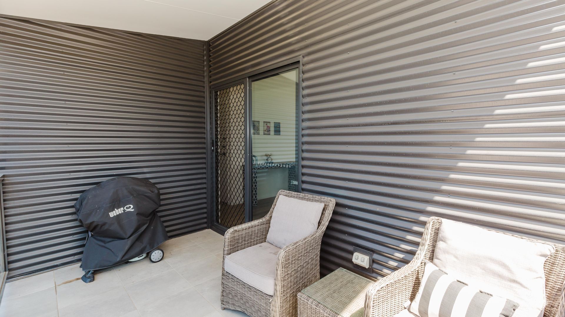 A balcony with a wicker chair, a small table, and a covered grill.