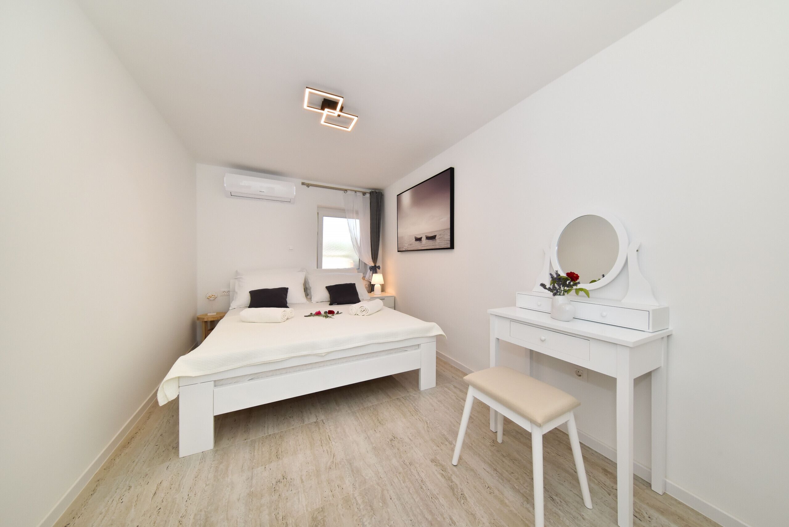 A bedroom with a bed, a vanity with a mirror, and a window.