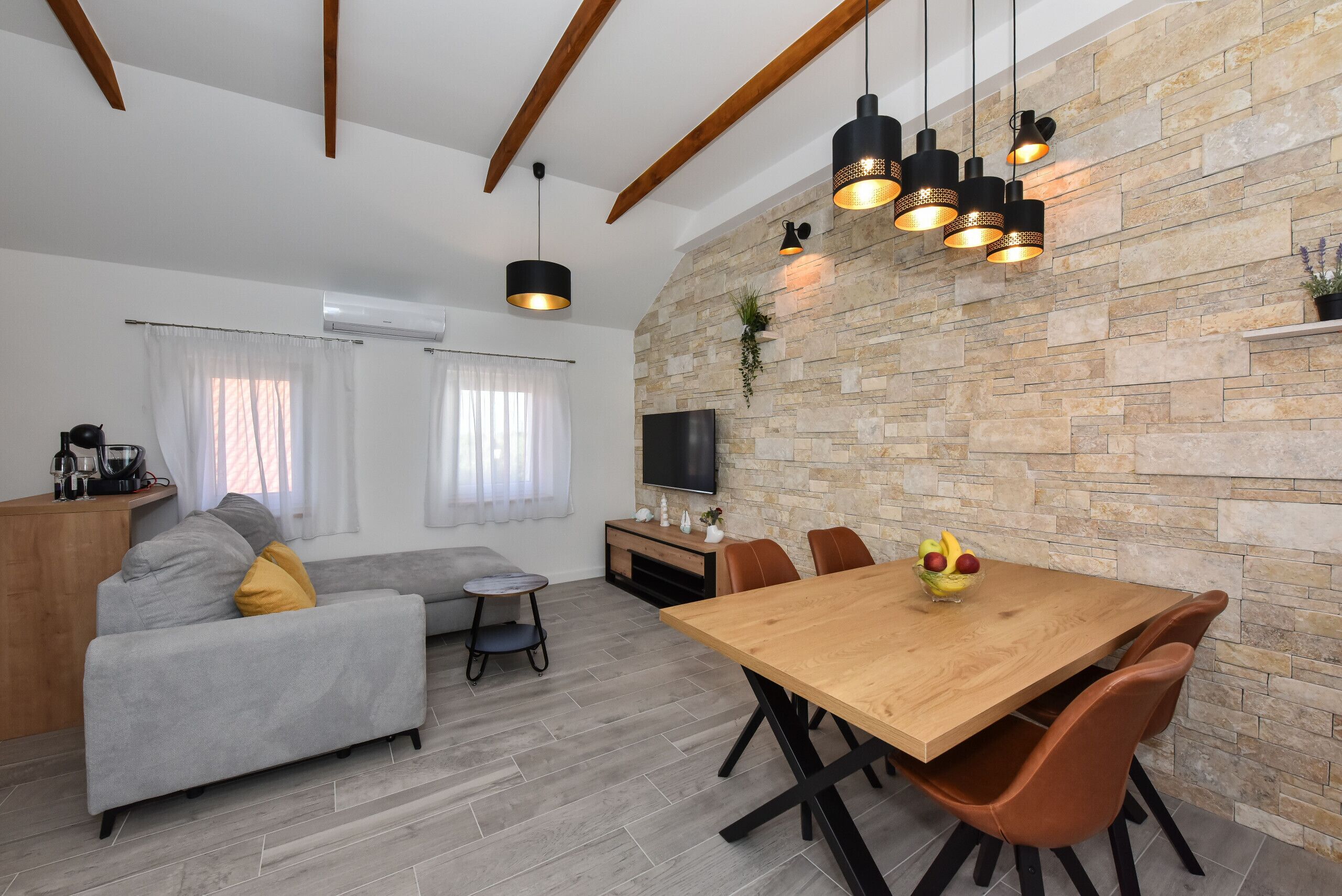A modern living room with a stone wall, a wooden dining table, and a grey sofa.