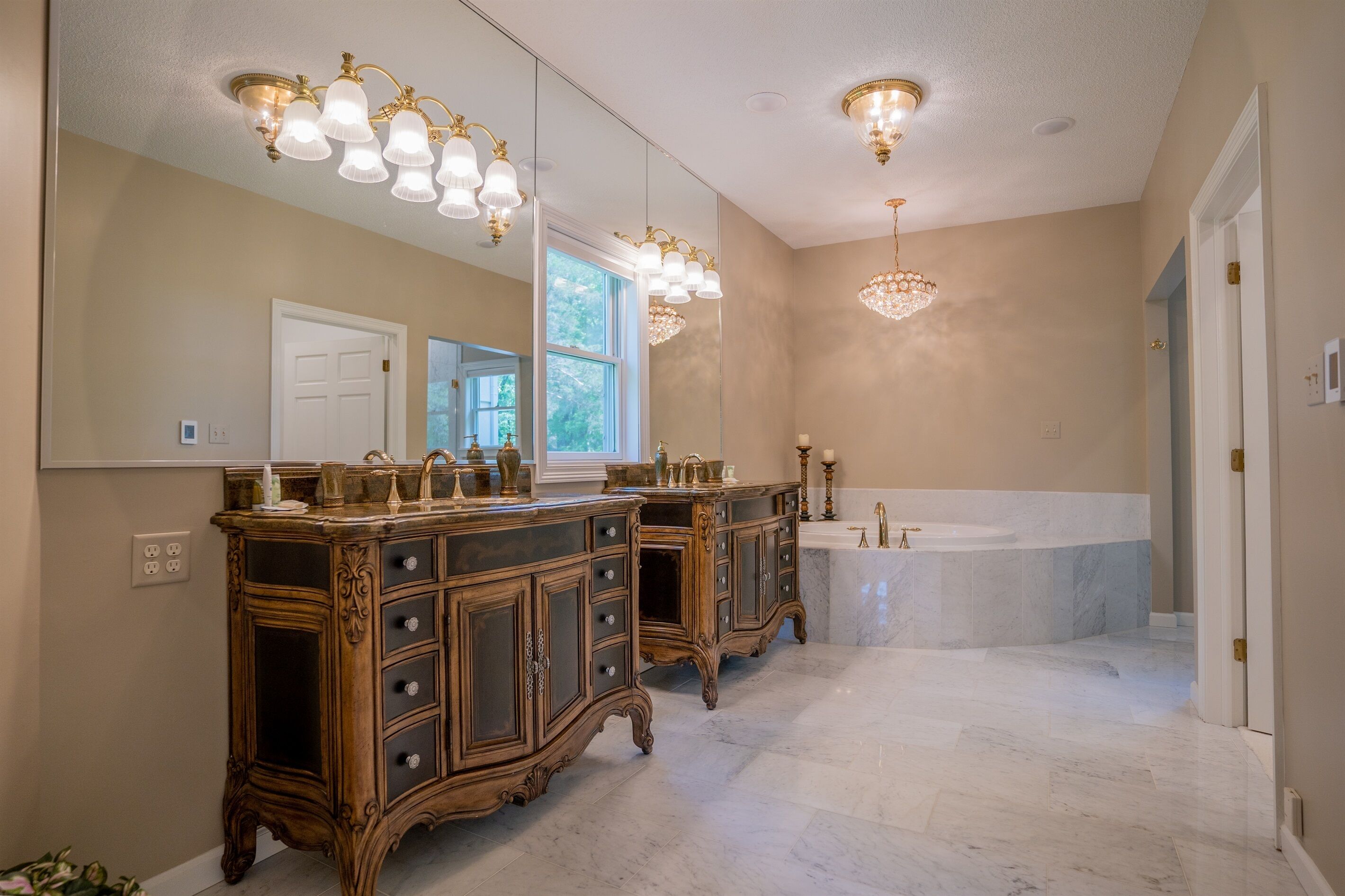 A bathroom with a large mirror, two sinks, a bathtub, and a chandelier.