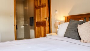 A bedroom with a wooden door, a bedside table with a lamp, and a bed with pillows. - Woodlawn (Kilmore)