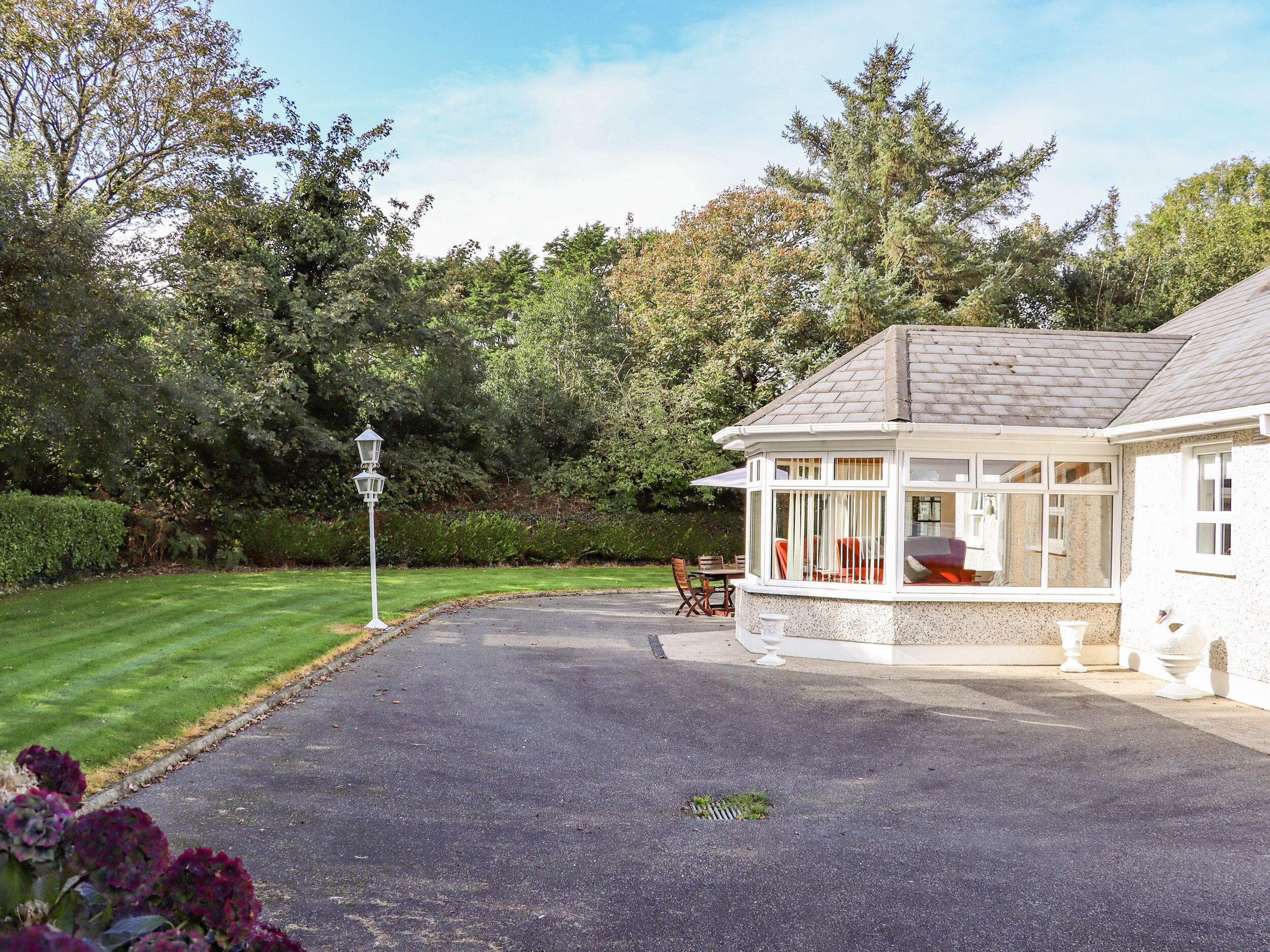 Ett hus med en inglasad veranda, en gräsmatta och en häck.