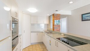 Une cuisine moderne avec des armoires blanches, un mur d’accent en briques, un four encastré, une cuisinière et un évier.