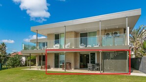 Une maison moderne à deux étages, dotée d’un balcon, de grandes fenêtres et d’un espace extérieur clôturé.