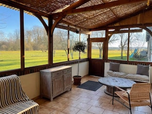 A covered outdoor seating area with a view of a grassy field and trees.