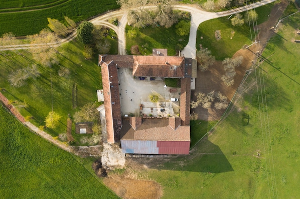 An aerial view of a farm with a large barn, a dirt road, and surrounding fields.