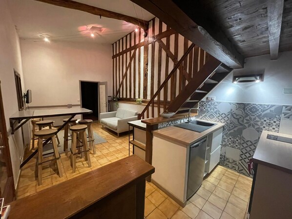 Una cocina con escalera de madera, comedor con taburetes y sofá blanco.