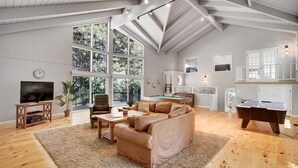 Un salon spacieux doté d’une grande fenêtre, d’une table de billard, d’un téléviseur et d’un coin salon confortable.