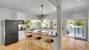 Une cuisine moderne dotée d’un grand îlot central, de chaises en bois et offrant une vue sur un lac par les fenêtres.