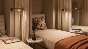 A hotel room with a bed, a bedside table with a magazine, a vase with reeds, and a mirror.