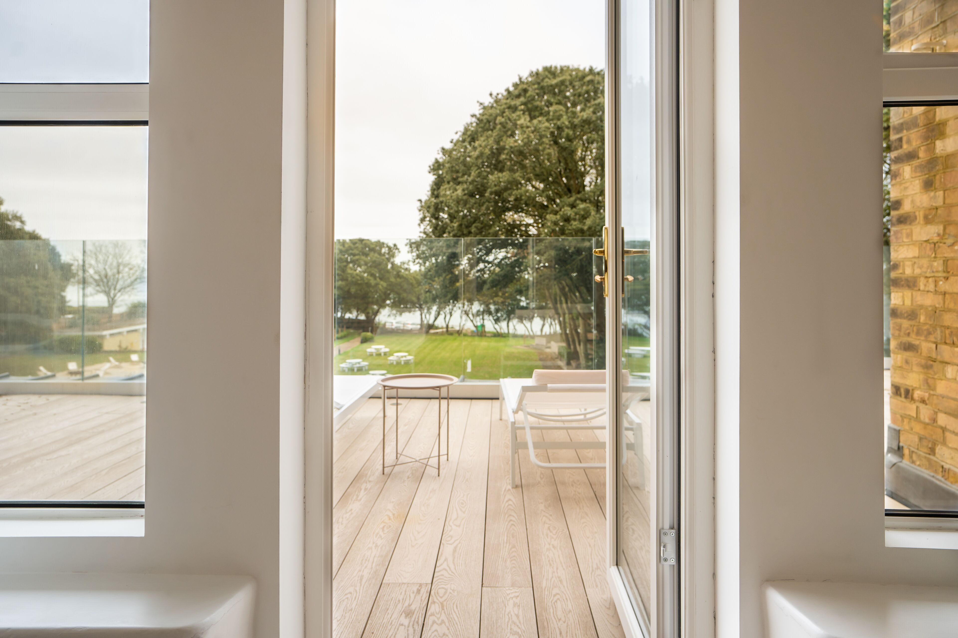 A modern room with a large sliding glass door leading to an outdoor deck with a wooden floor, a small round table, and a bench.