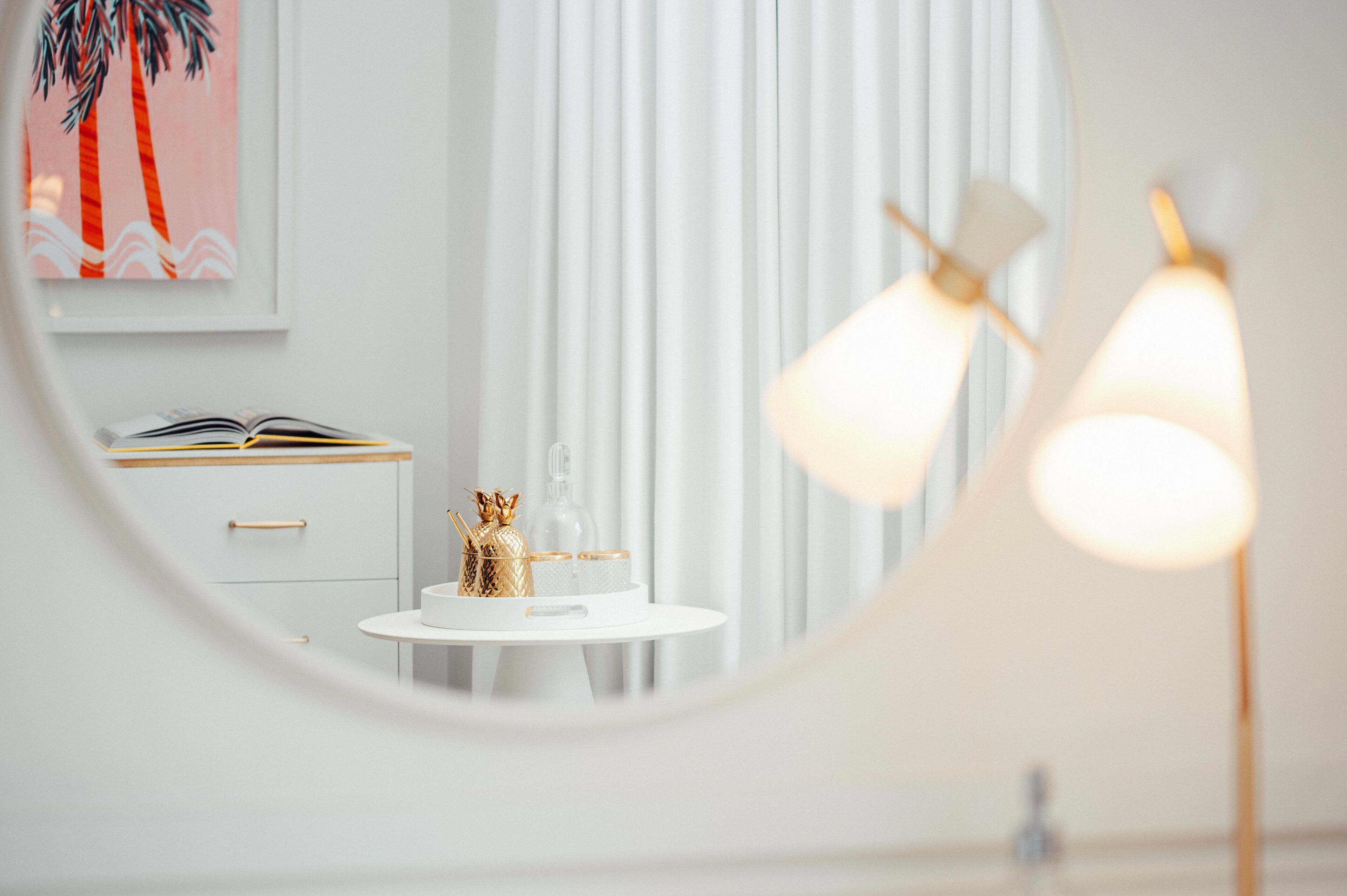 A modern bathroom with a round mirror, a white vanity, and a small table with decorative items.
