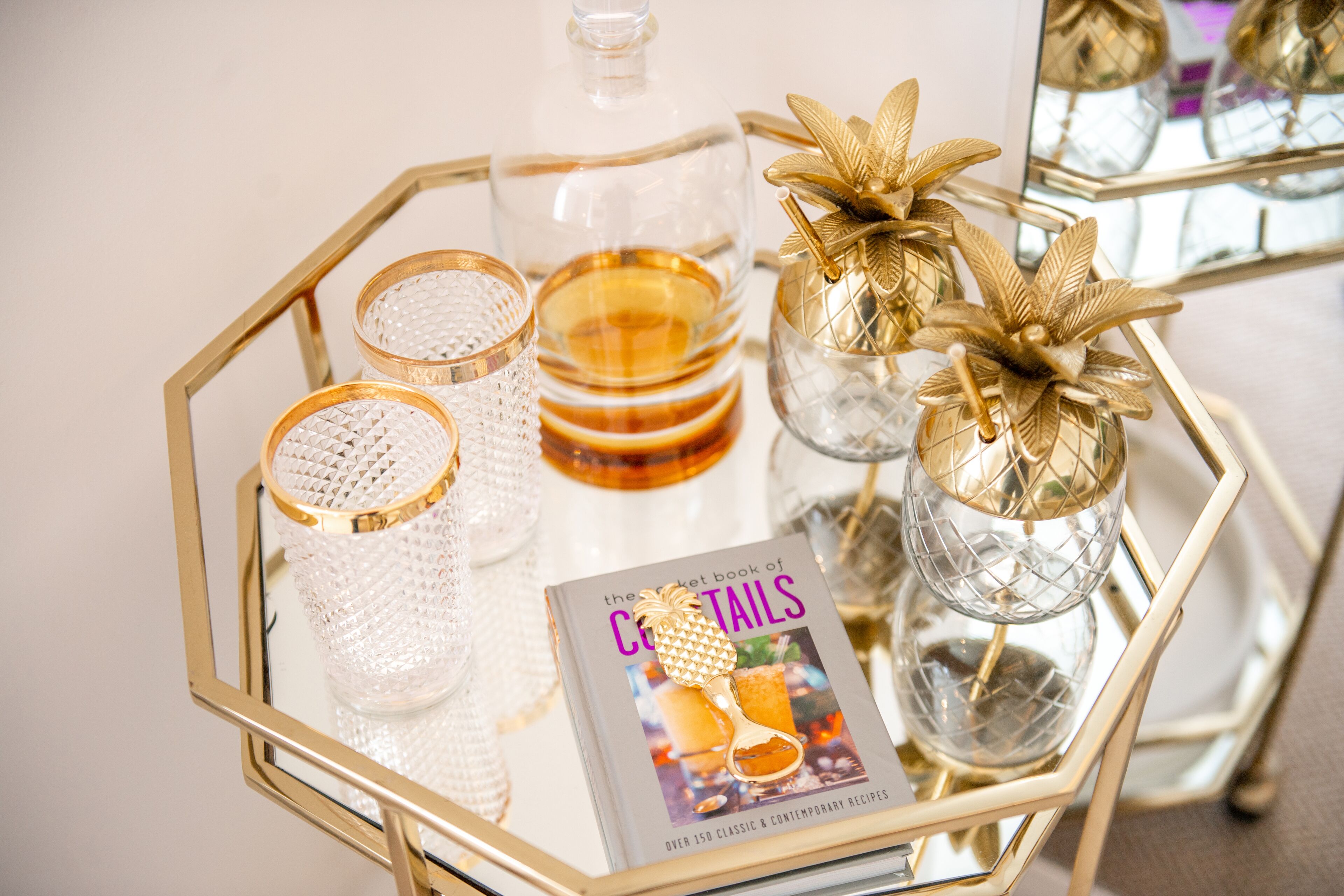 A tray with a book titled "The Cocktail Book of Cocktails" and various glassware and decorative items.