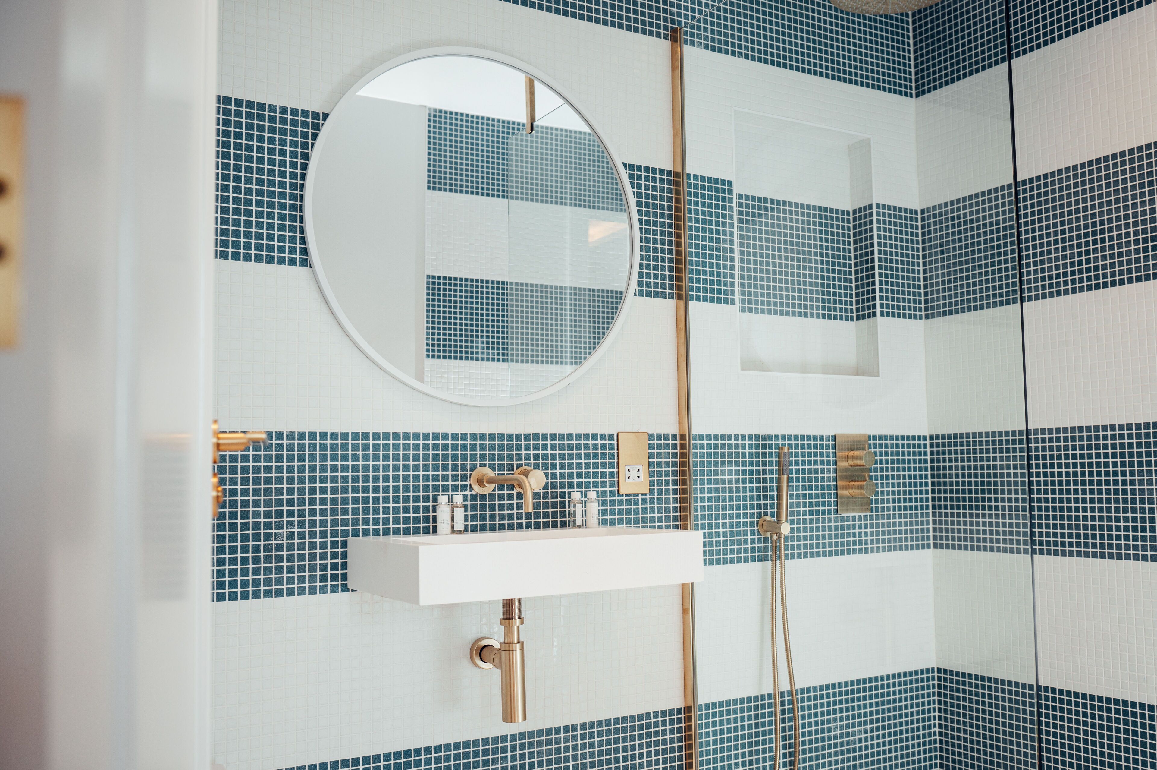 A bathroom with a round mirror, a sink, and a shower area.