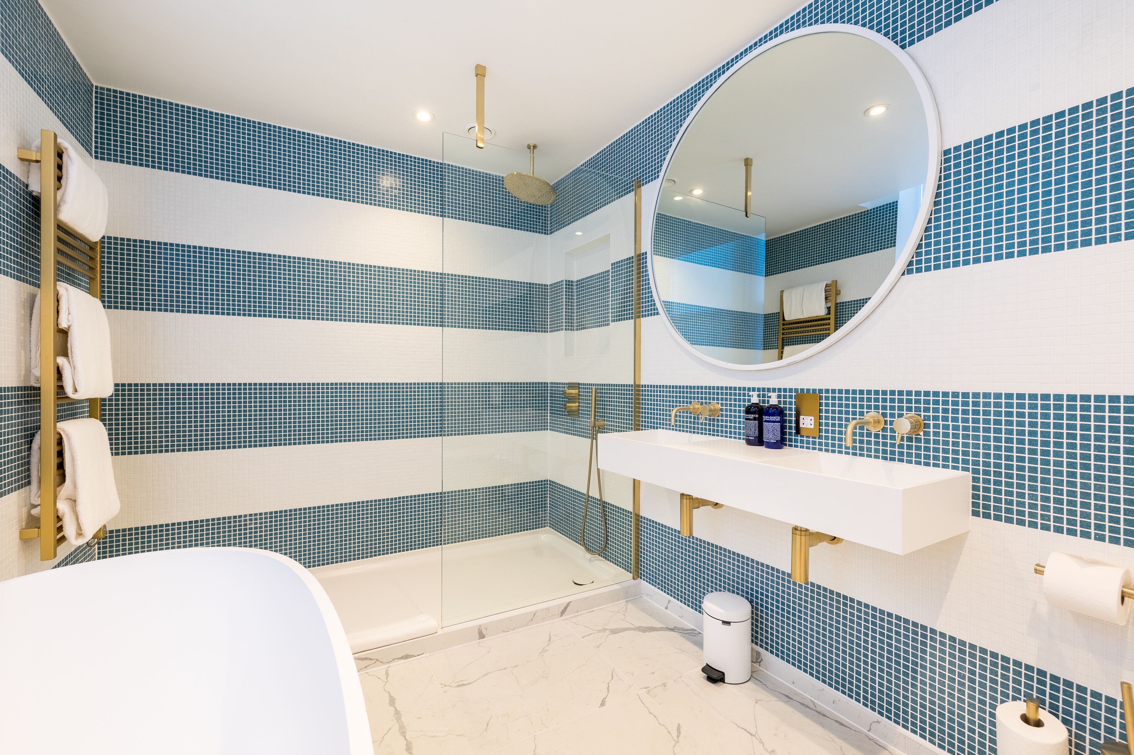 Une salle de bain moderne avec une douche à parois de verre, un lavabo blanc doté de robinetterie dorée et des murs recouverts de carreaux bleus.