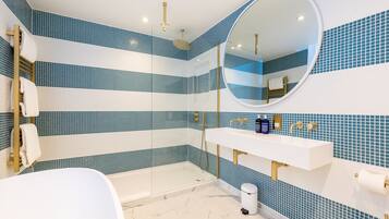 A modern bathroom with a glass-enclosed shower, a white sink with gold fixtures, and blue-tiled walls.