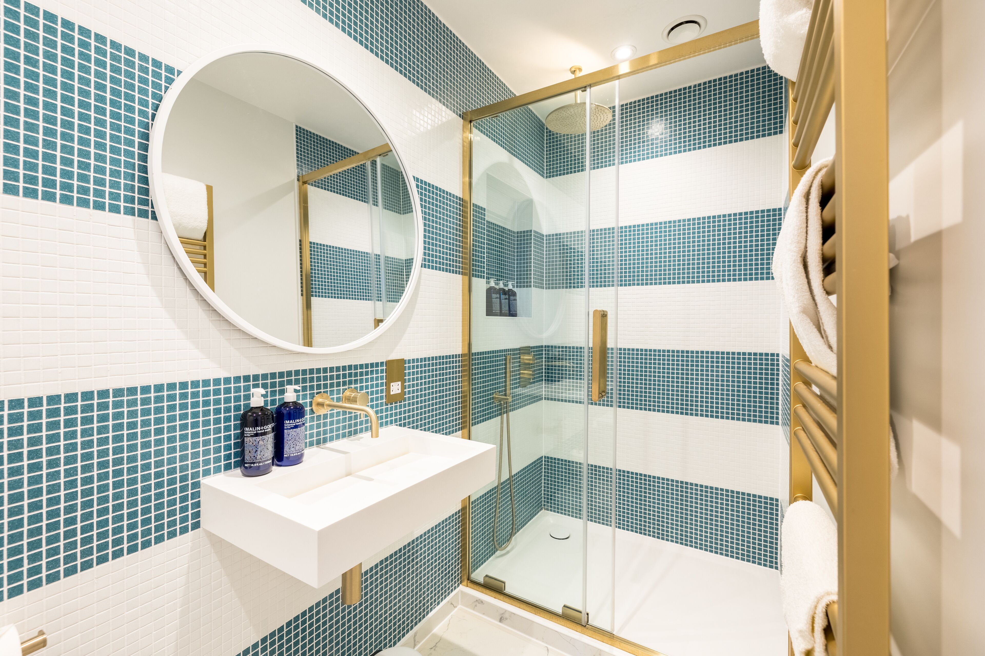 A bathroom with a white sink, a round mirror, and a glass-enclosed shower.