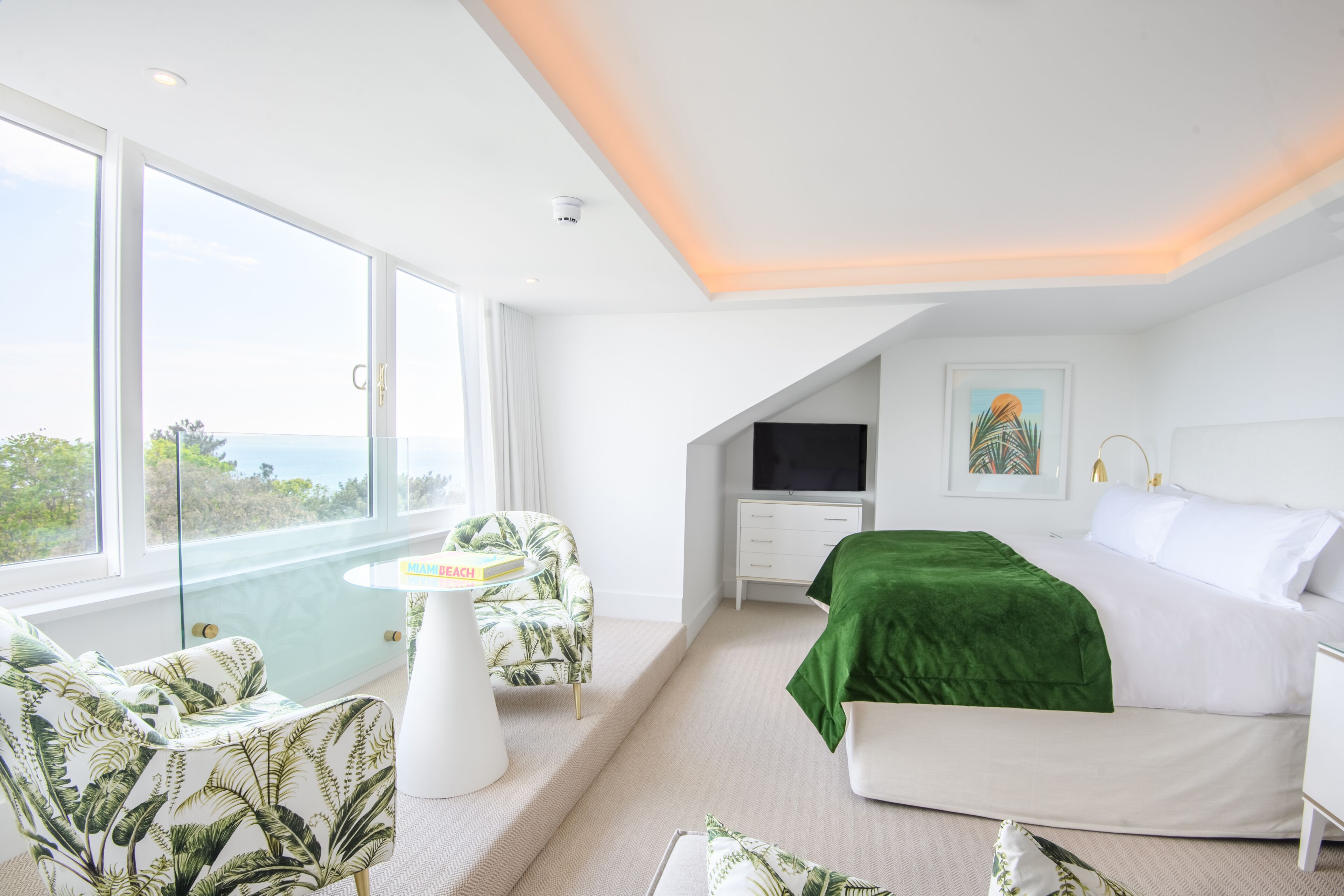A modern bedroom with a large bed, a TV, and a view of the ocean.