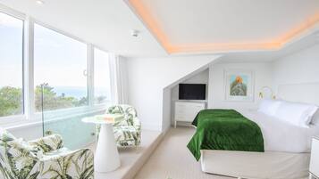 A modern bedroom with a large bed, a TV, and a view of the ocean.