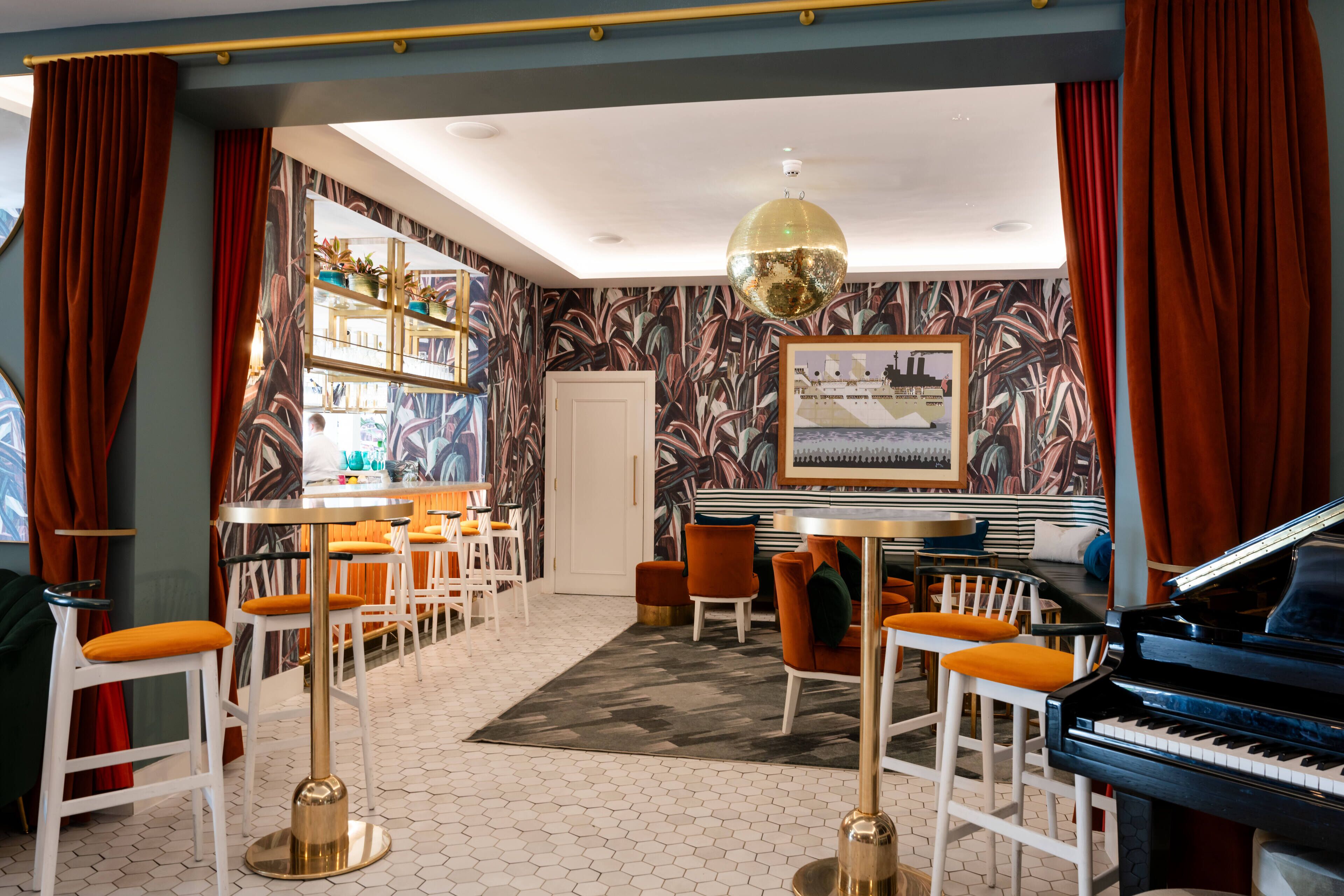 Uma área de bar com piano, banquetas e um espelho grande.