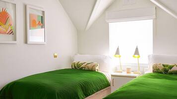 Un dormitorio con dos camas, ropa de cama verde, una ventana con contraventanas blancas y dos lámparas de noche.