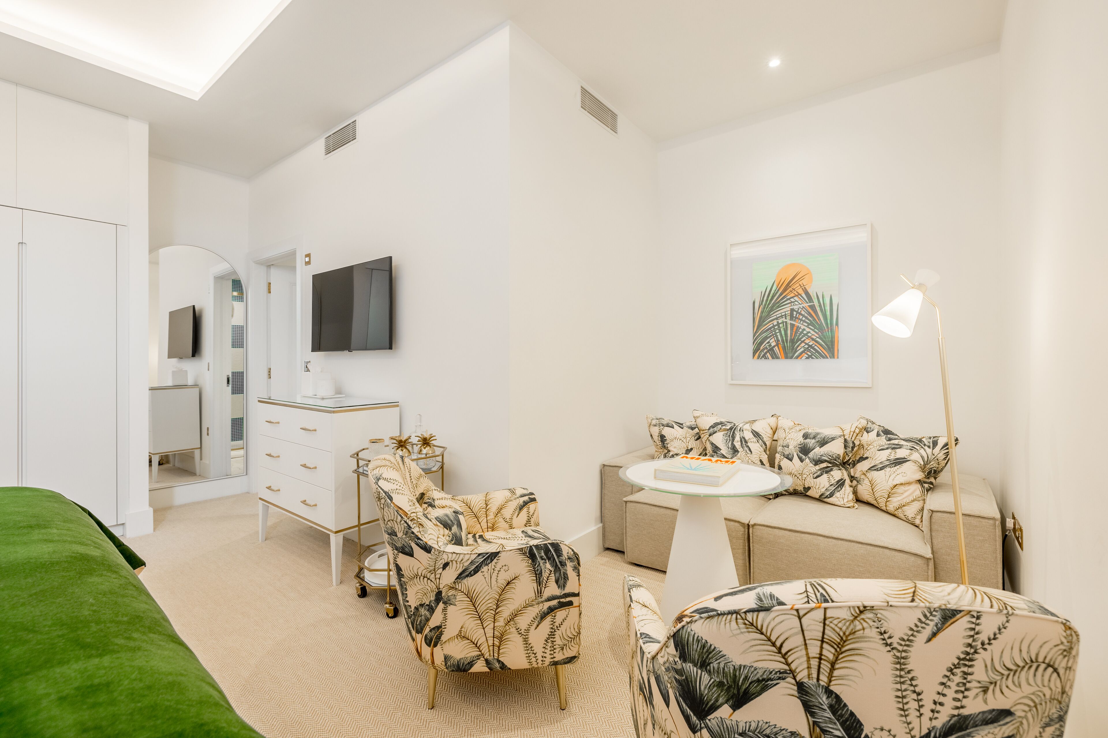 A modern bedroom with a bed, a vanity, a sofa, and a television.