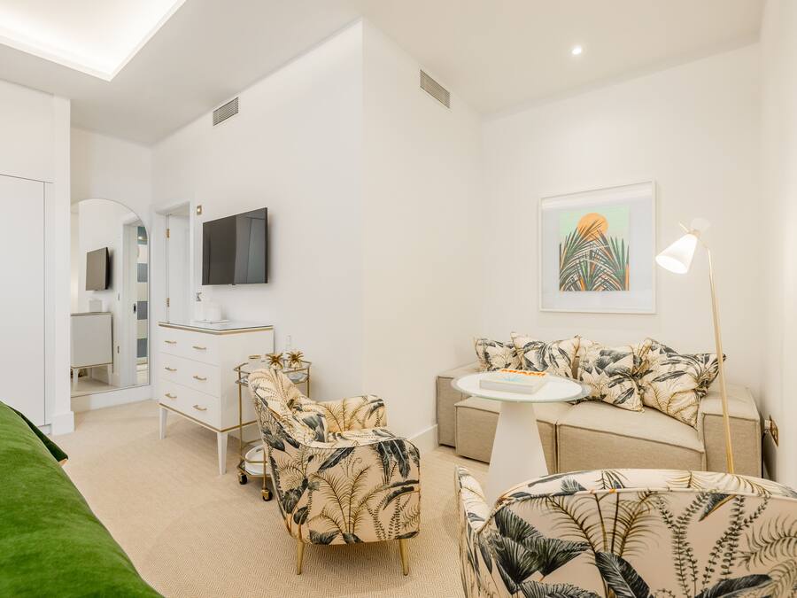 A modern bedroom with a bed, a vanity, a sofa, and a television.