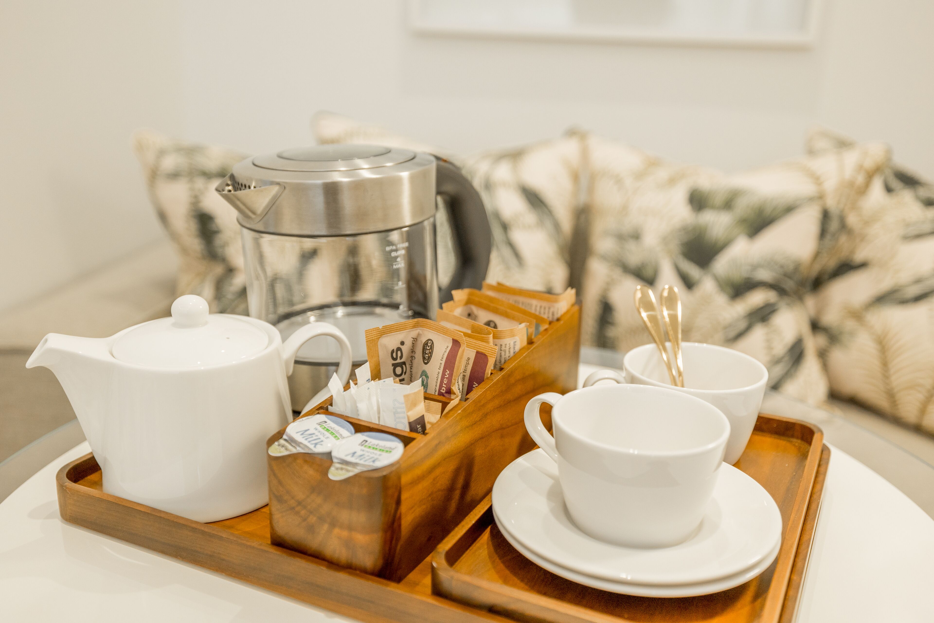 A tray with a white teapot, a coffee maker, a wooden box with tea packets, and two white cups on a tray.