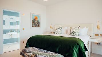 A modern bedroom with a large bed, a green velvet bedspread, a patterned bench, a white bedside table with a lamp, and a wall art piece.