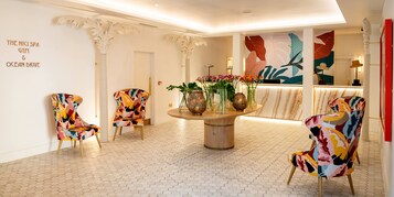 A lobby with a round table, colorful chairs, and a wall with a large leaf mural.