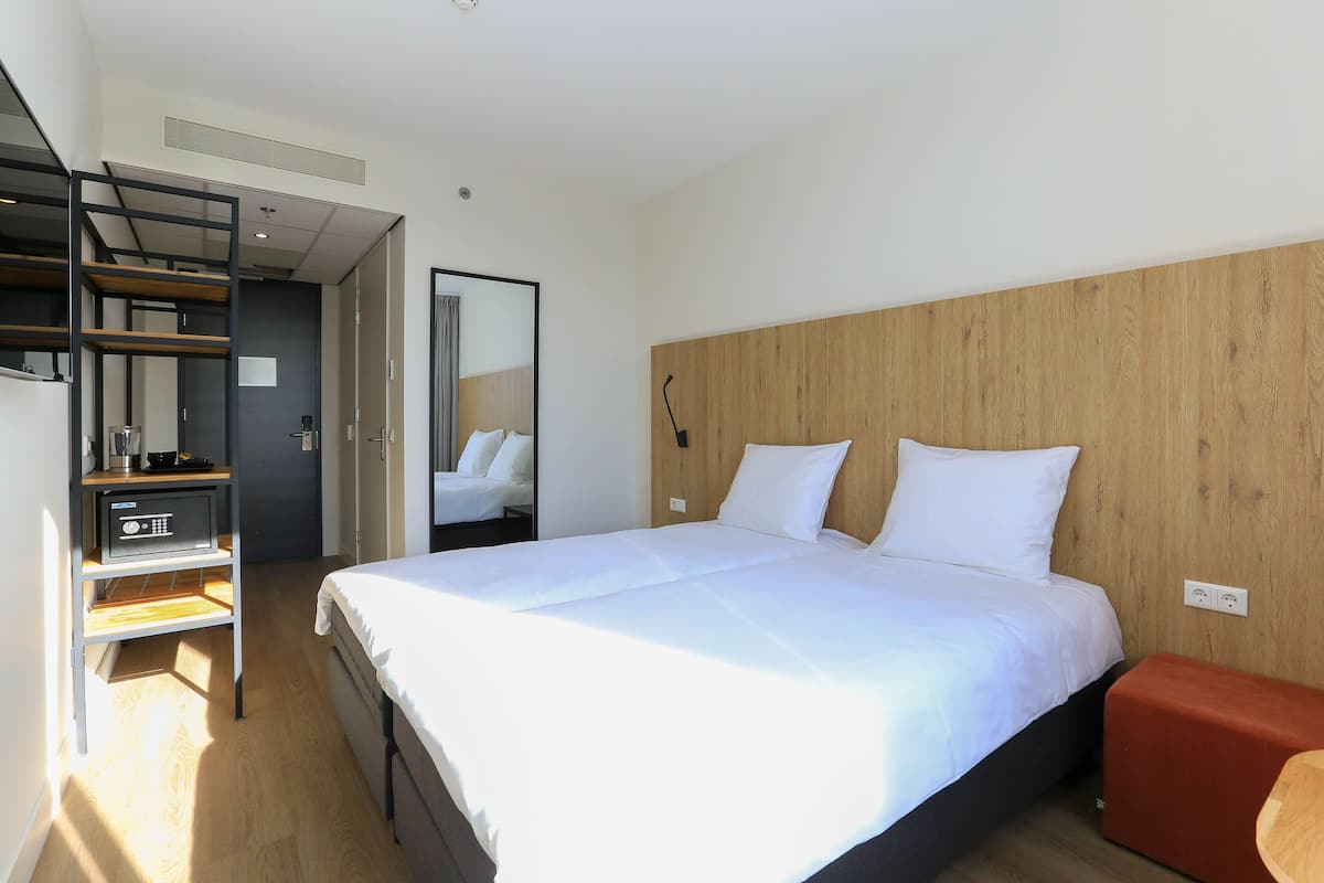 A hotel room with a large bed, a wooden headboard, a red bench, and a small table with a radio.