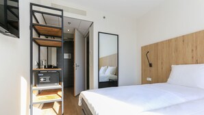 Une chambre d’hôtel avec un lit, une tête de lit en bois, une étagère avec une radio et une porte donnant sur une salle de bain.