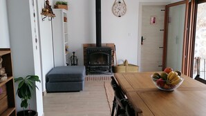 Un salon moderne avec une cheminée, des meubles en bois et un coin repas agrémenté d’un panier de fruits.