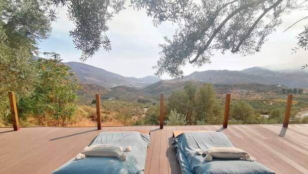 Deux lits en bois, recouverts de draps bleus, sur une terrasse extérieure offrant une vue sur un paysage montagneux.