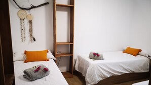 Une chambre avec deux lits, chacun agrémenté de draps blancs et d’oreillers orange, une étagère en bois et un élément décoratif mural.