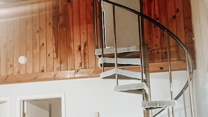 A spiral staircase with metal railings in a room with wooden walls and a white door.