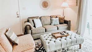 A living room with a sofa, ottoman, and a lamp.