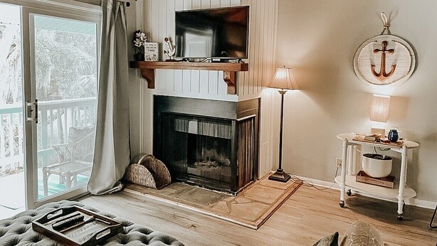 A cozy living room with a fireplace, a television on a wooden shelf, a lamp, and a decorative anchor on the wall.