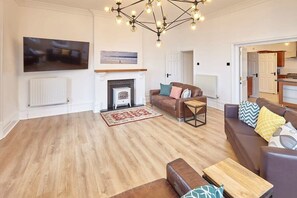 Ein geräumiges Wohnzimmer mit Kamin, großem Fernseher und einer modernen Chandelier.